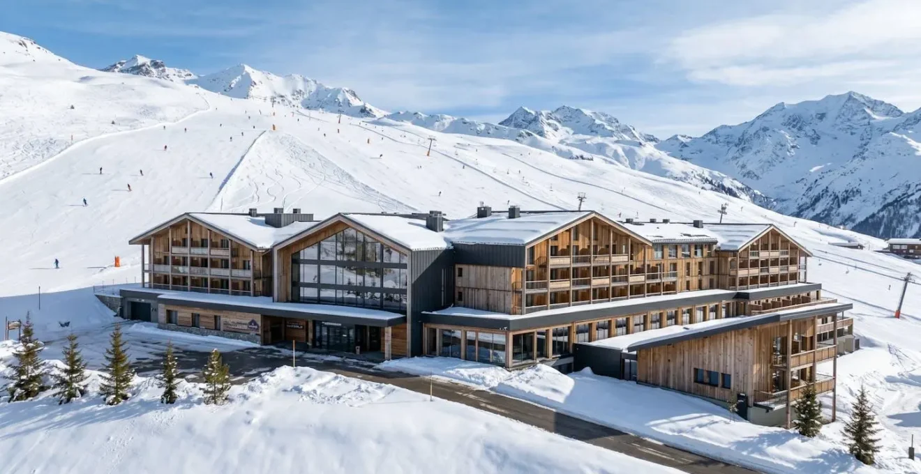 Vue extérieure d'une résidence de montagne à l'architecture alpine contemporaine, avec des skieurs visibles en arrière-plan sur les pistes enneigées