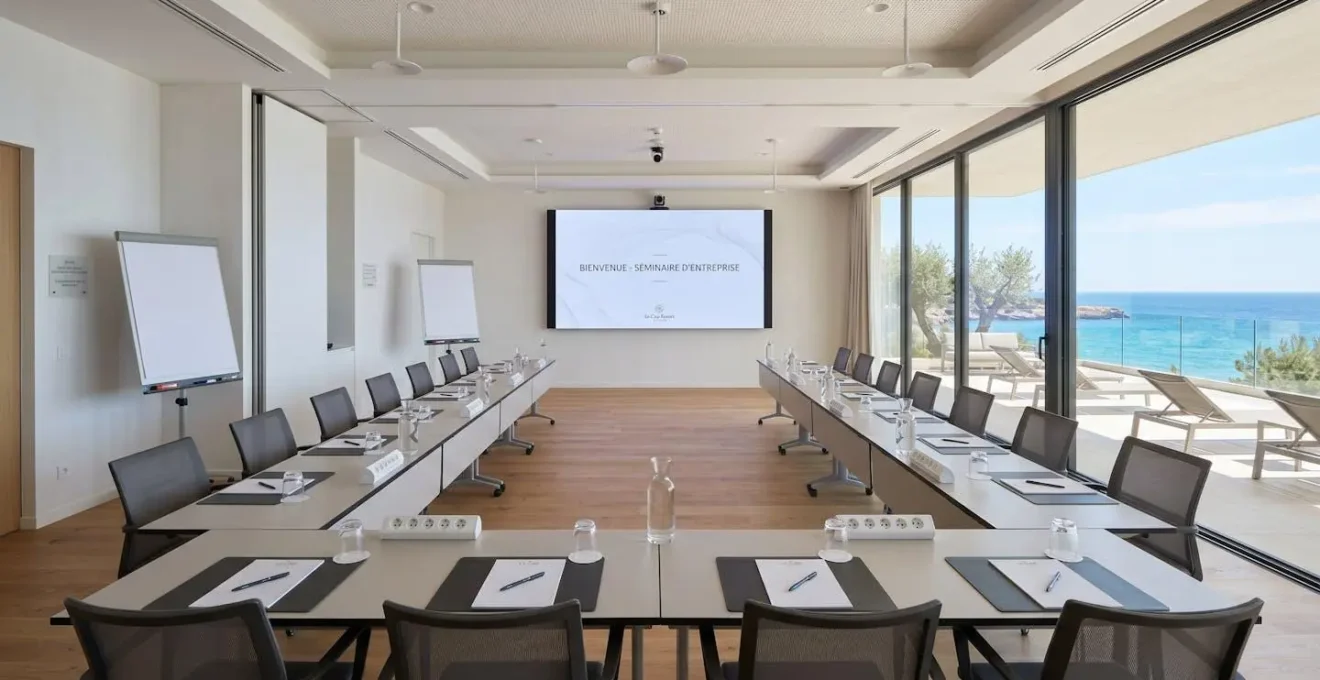 Salle de séminaire moderne avec configuration tables en U, écran LED et équipement audiovisuel, baie vitrée ouvrant sur panorama maritime méditerranéen